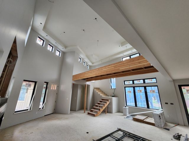 A double-height great room finished in white, with a stained timber beam, an open staircase and black-framed windows.