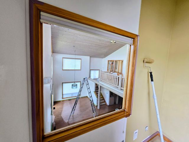 Interior repaint underway, with a freshly rolled cream wall beside an interior window looking through to the great room.
