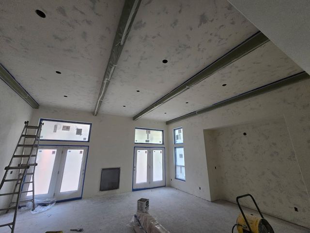 Great room masked off and prepped, ceiling beams and window trim taped ahead of the first coat.